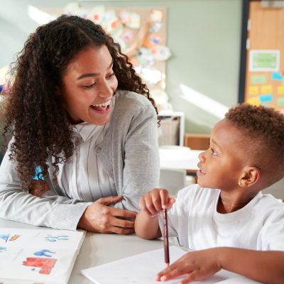 female-infant-school-teacher-working-one-one-with-young-schoolboy-sitting-table-smiling-each-other-close-up.jpg